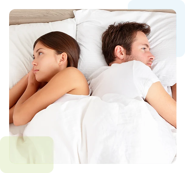 Upset young couple lying side by side in bed facing in opposite directions ignoring one another.